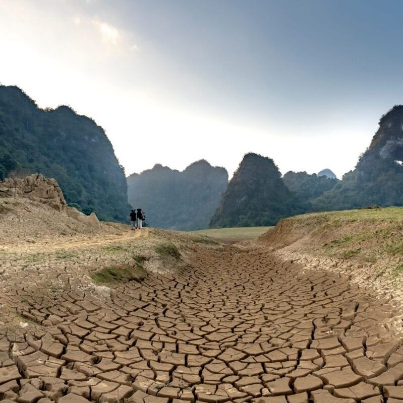 A wide shot of cracked earth with lush mountain backdrop, highlighting drought